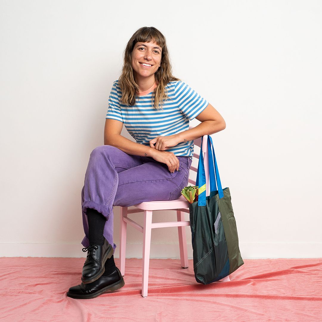 women with brown hair sitting on a pink chair wearing blue striped shirt and purple pants.